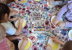 Na tym zdjęciu widać dzieci, które tworzą emotikony z jednorazowych talerzyków przedstawiające dwie emocje: smutek i radość.