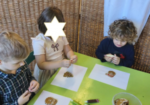 Zdjęcie przedstawia Mikołaja, Adasia i jedną z dziewczynek z grupy III ozdabiających pierniczki.