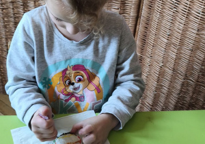 Na tym zdjęciu widać Oliwię z grupy III ozdabiającą lukrem wefelek ryżowy, tworząc bombkę