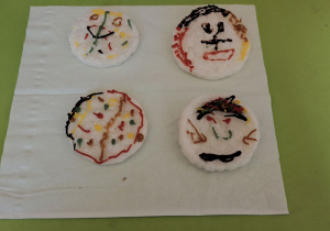 Zdjęcie przedstawia gotowe bombki wykonane przez dzieci z wafli ryżowych ozdobionych pisakami lukrowymi.