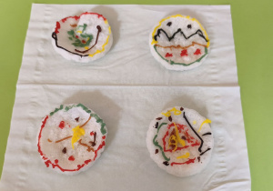 Zdjęcie przedstawia gotowe bombki wykonane przez dzieci z wafli ryżowych ozdobionych pisakami lukrowymi.