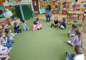 Zdjęcie przedstawia siedzace w kole dzieci i panią bibliotekarkę czytajacą książkę.