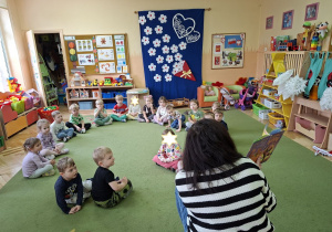 Zdjęcie przedstawia siedzace w kole dzieci i panią bibliotekarkę czytajacą książkę.