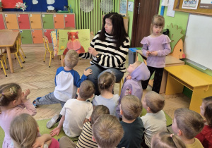 Na tym zdjęciu widać panią bibliotekarkę czytającą książkę oraz słuchające opowieści dzieci.