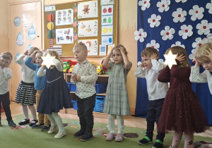 Zdjęcie przedstawia kilkoro dzieci śpiewajacych piosenkę połączoną z ilustracją ruchową.