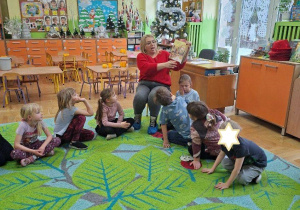 Zdjęcie przedstawia panią bibliotekarkę czytającą książkę oraz słuchające opowiadania dzieci.