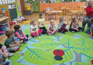 Zdjęcie przedstawia panią bibliotekarkę czytającą książkę oraz słuchające opowiadania dzieci.