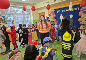 Zdjęcie przedstawia dzieci z grupy IV oraz kilkoro dzieci z grupy I podczas zabawy w korowodach.