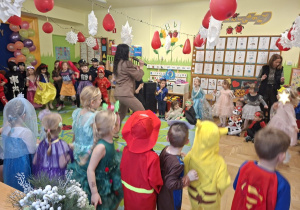 Na tym zdjęciu widać dzieci biorące udział w zabawach karnawałowych przy muzyce prowadzonych przez wodzirejkę.