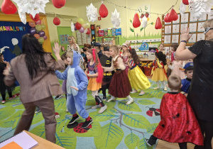 Na tym zdjęciu widać dzieci biorące udział w zabawach karnawałowych przy muzyce prowadzonych przez wodzirejkę.