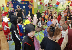 Na tym zdjęciu widać dzieci biorące udział w zabawach karnawałowych przy muzyce prowadzonych przez wodzirejkę.