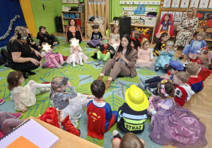 Na tym zdjęciu widać dzieci biorące udział w zabawach karnawałowych przy muzyce prowadzonych przez wodzirejkę.