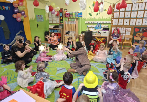 Na tym zdjęciu widać dzieci biorące udział w zabawach karnawałowych przy muzyce prowadzonych przez wodzirejkę.