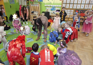 Na tym zdjęciu widać dzieci biorące udział w zabawach karnawałowych przy muzyce prowadzonych przez wodzirejkę.