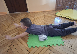 Zdjęcie przedstawia Maksa z grupy II wykonującego ćwiczenie wzmacniające górną część pleców oraz poprawiające postawę ciała.