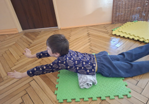 Zdjęcie przedstawia Adasia M. z grupy II wykonującego ćwiczenie wzmacniające górną część pleców oraz poprawiające postawę ciała.