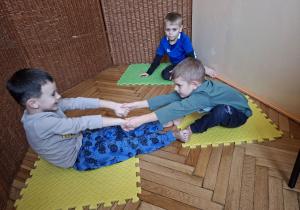 Zdjęcie przedstawia trzech chłopców z grupy III wykonujących ćwiczenia wiloznaczne, ogólnorozwojowe w parach.