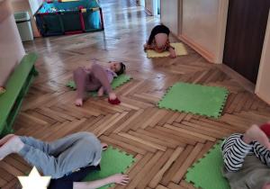 Zdjęcie przedstawia czworo dzieci z grupy IV wykonujących ćwiczenie angażujące dolne partie mięśni brzucha oraz wzmacjające dolny odcinek pleców.