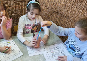 Zdjęcie przedstawia trzy dziewczynki wykonujace karty pracy z elementami do piramidy zdrowego żywienia.