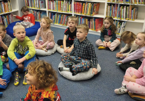 Zdjęcie przedstawia dzieci siedzące na pufach w czytelni w bibliotece.