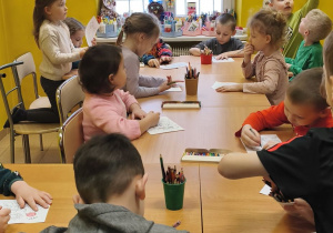 Zdjęcie przedstawia dzieci siedzące przy stolikach w czytelni i kolorujące malowanki.