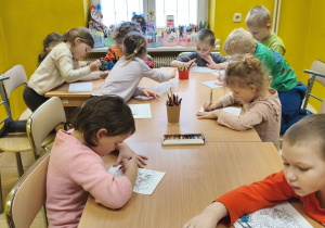 Zdjęcie przedstawia dzieci siedzące przy stolikach w czytelni i kolorujące malowanki.