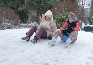 Zdjęcie przedstawia Marcelinkę T. i Mayę zjeżdżające na jabłuszkach z górki.