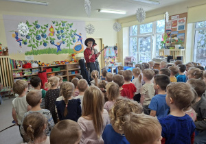 Na tym zdjęciu widać prowadzących koncert oraz dzieci podczas wspólnej zabawy przy dźwiękach gitary.