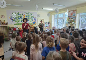 Na tym zdjęciu widać prowadzących koncert oraz dzieci podczas wspólnej zabawy przy dźwiękach gitary.