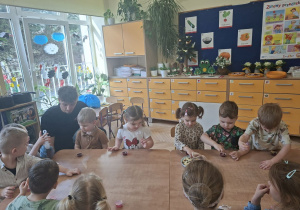 Zdjęcie przedstawia dzieci siedzące przy stolikach i ozdabiające pralinki.