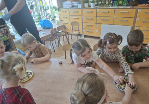 Zdjęcie przedstawia kilkoro dzieci ozdabiających sowje czekoladki.