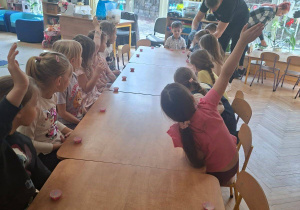 Zdjęcie przedstawia dzieci siedzące przy stolikach podczas zajęć.