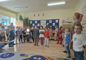 Zdjęcie przedstawia Adasia M., Lilę oraz Tymka recytujących wiersz oraz pozostałe dzieci z grupy III.