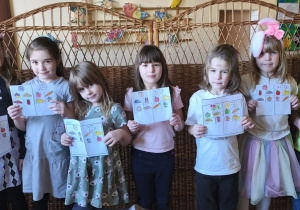 Zdjęcie przedstawia pięć dziewczynek i dwóch chłopców z grupy IV prezentujących wykonane przez siebie karty pracy.