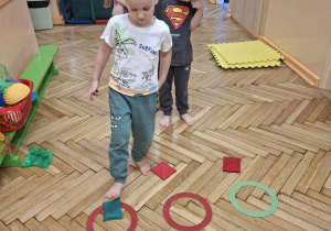 Zdjęcie przedstawia troje dzieci z grupy II wykonujących ćwiczenia przeciw płaskostopiu z przyborem.