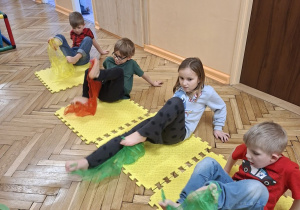 Zdjęcie przedstawia dzieci z grupy IV wykonujące ćwiczenie wzmacniające mięsnie brzucha oraz stopy z chustką