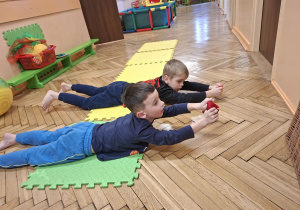 Zdjęcie przedstawia Marcela i Wojtka z grupy III wykonujących ćwiczenie z przyborem wzmacniające plecy, barki, a także stabilizujące kręgosłup.