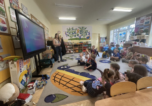 Na tym zdjęciu widać dzieci z grupy III oraz prowadzącą warsztaty, która wyjaśnia dzieciom z grupy III, co będą robiły na warsztatach.