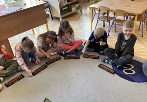 Zdjęcie przedstawia kilkoro dzieci z grupy III, które uczą się, jak pracować z sorobanem.