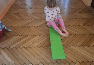 Na tym zdjęciu widać Lenę R. z grupy I wykonującą przenoszenie woreczka stopami na drugą stronę ławeczki.