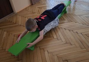 Zdjęcie przedstawia Wojtka z grupy III wykonującego przeciąganie po ławeczce w leżeniu przodem.
