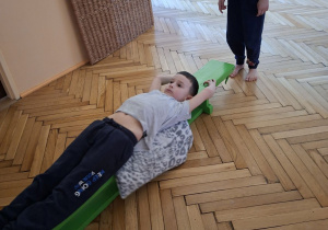 Zdjęcie przedstawia Marcela z grupy III wykonującego przeciąganie po ławeczce w leżeniu tyłem.