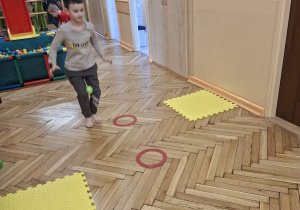 Zdjęcie przedstawia Marcela z grupy III podczas wykonywania slalomu między krążkami z piłeczką trzymaną kolanami.