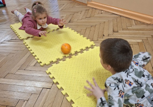 Na tym zdjęciu widać Jagodę L. i Adasia M. z grupy II toczących piłeczkę nawzajem do siebie w leżeniu przodem.