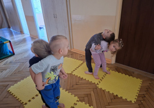 Zdjęcie przedstawia Kubę S., Jagodę l., Maksa Z. z grupy II i Henia D. z grupy I wykonujących ćwiczenie w parach w staniu tyłem do siebie - przeciąganie.