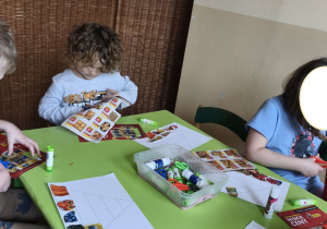 Zdjęcie przedstawia Adasia M. i Mikołaja z grupy III z koleżanką wycinających obrazki do piramidy zdrowia.