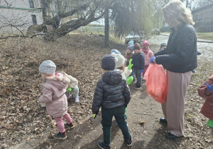 Zdjęcie przedstawia dzieci porządkujące teren w okolicy przedszkola.
