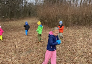 Zdjęcie przedstawia dzieci porządkujące teren parku w pobliżu przedszkola.