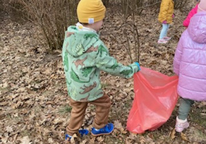 Zdjęcie przedstawia dzieci porządkujące teren parku w pobliżu przedszkola.