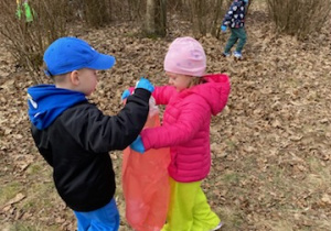 Zdjęcie przedstawia dzieci porządkujące teren parku w pobliżu przedszkola.